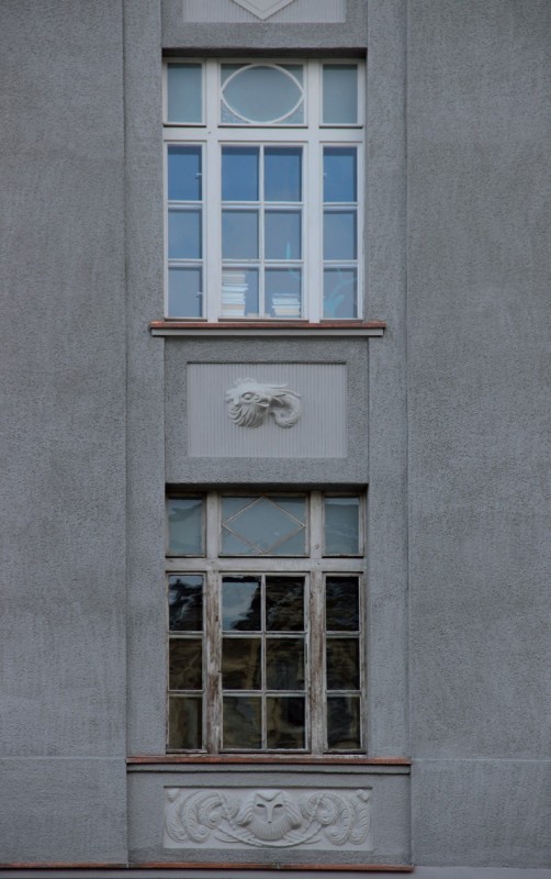 Zbliżenia na okienną stolarkę gmachu z motywami klasycystycznej ornamentyki.