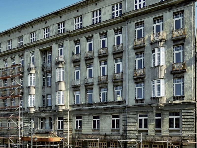 Elewacja frontowa hotelu przed rozpoczęciem prac. W świetle bocznym (prawa krawędź obrazu widoczny stan i struktura tynków pokrytych cementowym szprycem.